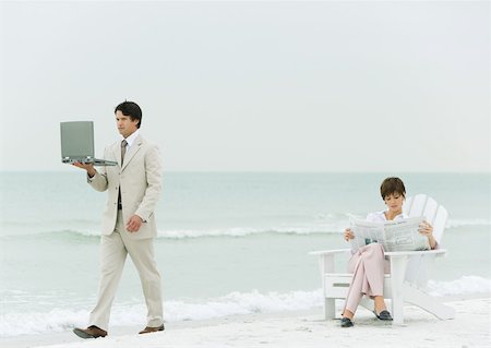 simsearch:632-01160695,k - On beach, businessman carrying laptop, walking by woman reading newspaper in chair Stock Photo - Premium Royalty-Free, Code: 632-01160299