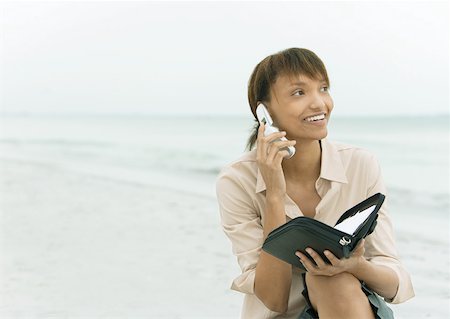 Woman using cell phone and holding agenda, sea in background Stock Photo - Premium Royalty-Free, Code: 632-01160304