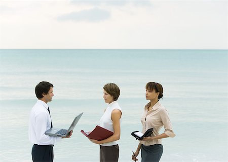 simsearch:632-03500777,k - Businessman holding laptop, facing women holding agendas, sea in background Foto de stock - Royalty Free Premium, Número: 632-01160302