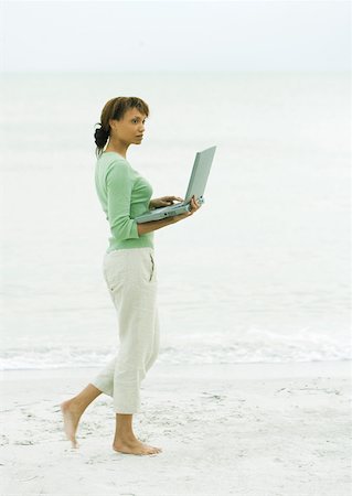 Woman walking on beach, carrying open laptop Stock Photo - Premium Royalty-Free, Code: 632-01160314