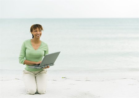 Woman on beach, kneeling on sand with laptop Stock Photo - Premium Royalty-Free, Code: 632-01160311