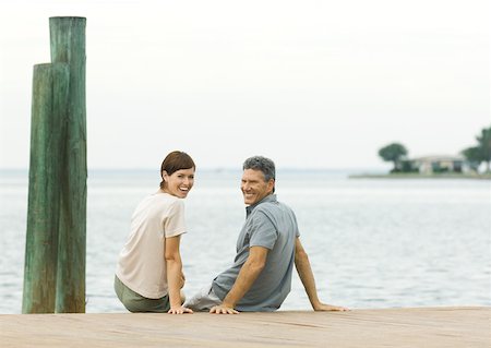 sit man backside view - Couple sitting on edge of dock, smiling over shoulders at camera Foto de stock - Sin royalties Premium, Código: 632-01161285