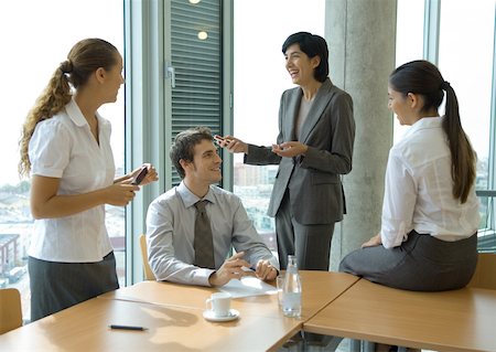 simsearch:695-05763908,k - Business colleagues standing at sitting at table, discussing Fotografie stock - Premium Royalty-Free, Codice: 632-01162487