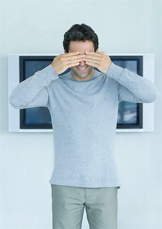 Man standing in front of widescreen TV on wall, hands covering eyes Stock Photo - Premium Royalty-Free, Code: 632-01194075