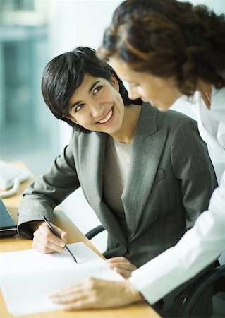 Woman sitting as desk, pointing to document and smiling at second woman Stock Photo - Premium Royalty-Free, Code: 632-01194128