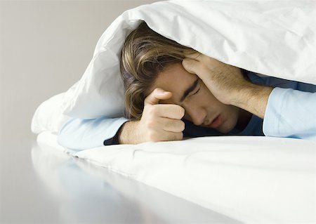 eiderdown duvet white - Man lying under covers, holding head Stock Photo - Premium Royalty-Free, Code: 632-01193857