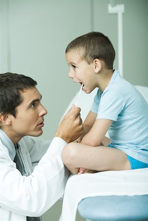 Doctor looking into boy's mouth with tongue depressor, side view Stock Photo - Premium Royalty-Free, Code: 632-01277176