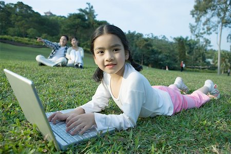 simsearch:632-01271089,k - Girl lying in grass using laptop, parents in background Stock Photo - Premium Royalty-Free, Code: 632-01270549