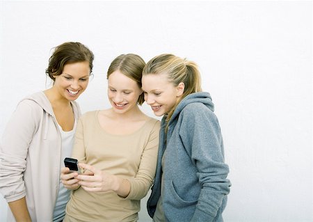simsearch:632-01271195,k - Three young female friends looking at cell phone together, smiling Fotografie stock - Premium Royalty-Free, Codice: 632-01270962