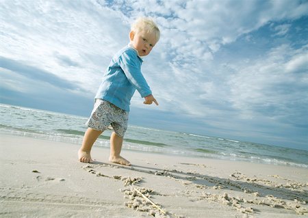 Toddler standing on beach, looking at camera and pointing at sand Foto de stock - Sin royalties Premium, Código: 632-01271278