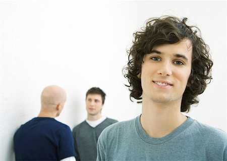 Young man smiling at camera, two young men talking in background Stock Photo - Premium Royalty-Free, Code: 632-01271472