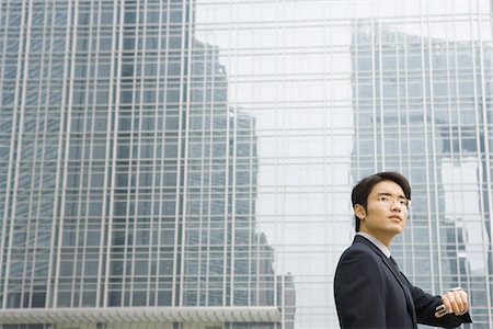 Young businessman holding up wrist to check time, looking away, office building in background Stock Photo - Premium Royalty-Free, Code: 632-01272015