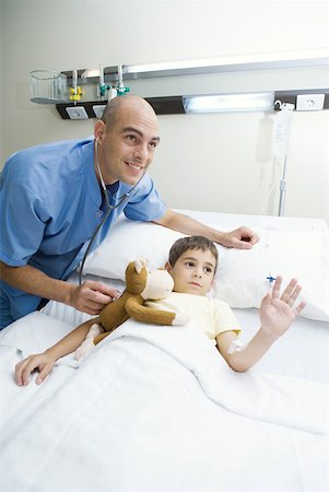 Boy lying in hospital bed, intern holding stethoscope to boy's stuffed animal, both looking out of frame Stock Photo - Premium Royalty-Free, Code: 632-01380265