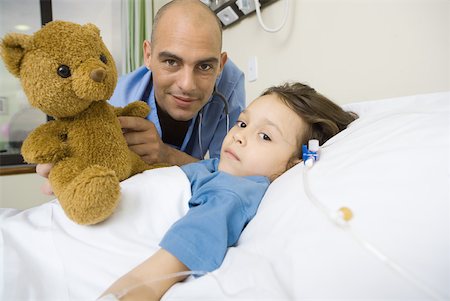 simsearch:632-01380299,k - Girl lying in hospital bed, male intern next to her holding up teddy bear Stock Photo - Premium Royalty-Free, Code: 632-01380299