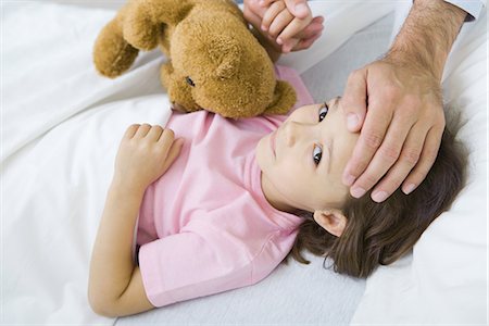 simsearch:632-01380299,k - Girl lying in bed with teddy bear, man holding her hand on putting other hand on her forehead Stock Photo - Premium Royalty-Free, Code: 632-01380301