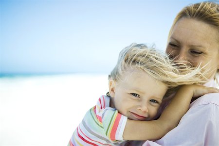 simsearch:695-03375963,k - Woman holding daughter on beach, girl smiling at camera as wind tousles her hair Stock Photo - Premium Royalty-Free, Code: 632-01380394