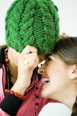 simsearch:632-01277233,k - Two young female friends with heads together, one pulling knit hat over eyes while the other laughs Fotografie stock - Premium Royalty-Free, Codice: 632-01380453