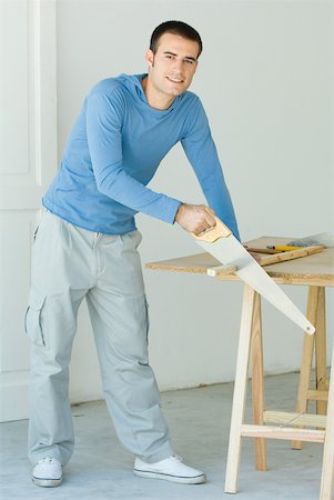 Man sawing piece of wood, looking at camera Stock Photo - Premium Royalty-Free, Code: 632-01380525