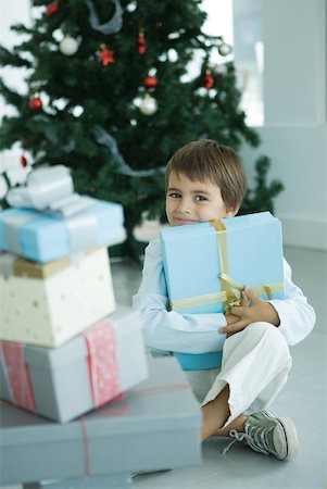 simsearch:640-02949371,k - Boy sitting next to stack of Christmas presents, holding one against chest Stock Photo - Premium Royalty-Free, Code: 632-01380610