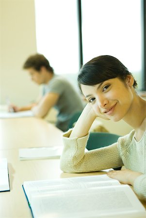 simsearch:632-01380712,k - Female college student sitting at table with book, smiling at camera Fotografie stock - Premium Royalty-Free, Codice: 632-01380709