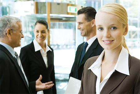 simsearch:695-03376535,k - Young businesswoman smiling at camera, associates chatting in background Stock Photo - Premium Royalty-Free, Code: 632-01612026