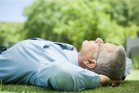 Mature businessman lying on ground outdoors, hands behind head, eyes closed, close-up Stock Photo - Premium Royalty-Free, Code: 632-01612158