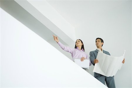 Woman and man standing with blueprints, woman pointing to distance, low angle view Stock Photo - Premium Royalty-Free, Code: 632-01612722