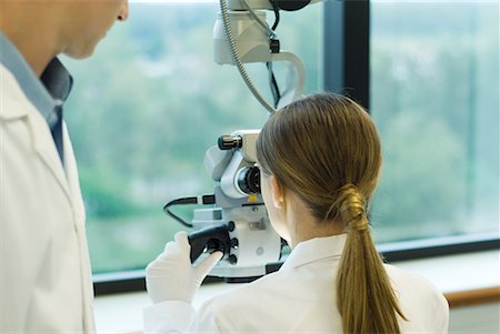 scientists standing together - Young woman using microscope while male colleague watches, rear view Stock Photo - Premium Royalty-Free, Code: 632-01612774