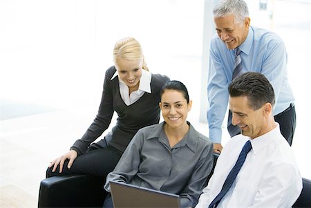 Business associates looking at laptop together, woman in center smiling at camera Stock Photo - Premium Royalty-Free, Code: 632-01612877
