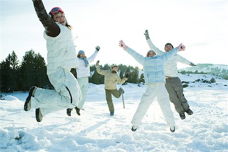 Young friends jumping in the air, dressed in winter clothing, smiling at camera Stock Photo - Premium Royalty-Free, Code: 632-01612972