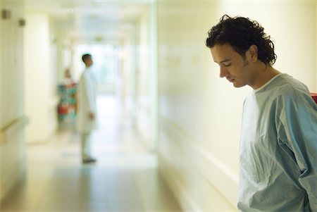 simsearch:632-01613047,k - Patient masculin debout dans le couloir de l'hôpital, regardant vers le bas, vue latérale Photographie de stock - Premium Libres de Droits, Code: 632-01613043