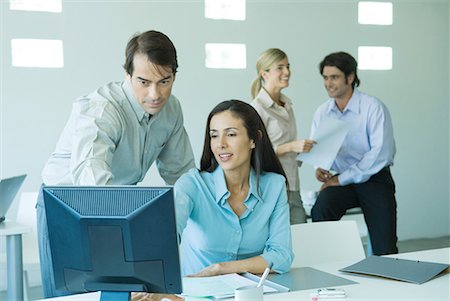 Businessman and businesswoman in office, looking at computer, associates in background Stock Photo - Premium Royalty-Free, Code: 632-01613108