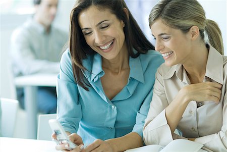 Two businesswomen looking at cell phone, smiling, waist up Stock Photo - Premium Royalty-Free, Code: 632-01613151