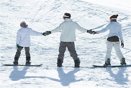 Three young snowboarders standing together, holding hands, rear view Stock Photo - Premium Royalty-Free, Code: 632-01613224