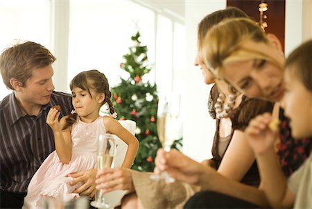 Family seated together, smiling, children eating snack, Christmas tree in background Stock Photo - Premium Royalty-Free, Code: 632-01613348