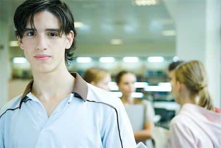 simsearch:632-03424176,k - Male student smiling at camera, portrait, peers in background Foto de stock - Sin royalties Premium, Código: 632-01613445