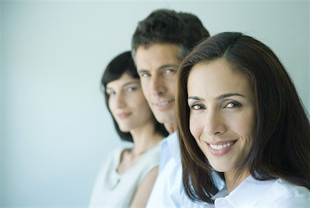 simsearch:632-03424176,k - Business team in a row smiling at camera, head and shoulders, focus on woman in foreground, portrait Foto de stock - Sin royalties Premium, Código: 632-01636787