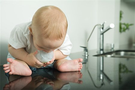 Baby sitting on kitchen counter, holding bottle, looking down at reflection Stock Photo - Premium Royalty-Free, Code: 632-01636894