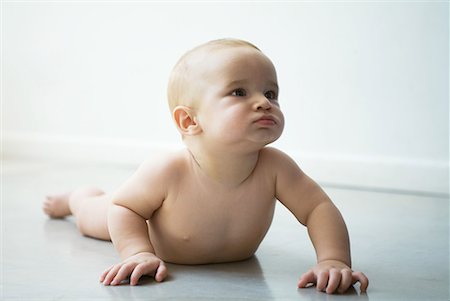 Baby lying on floor, lifting self up with arms, looking away, full length Stock Photo - Premium Royalty-Free, Code: 632-01636931