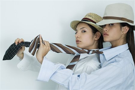 Two young female friends dressed in button down shirts, ties and hats, holding out ties, glancing at camera, portrait Foto de stock - Royalty Free Premium, Número: 632-01638401
