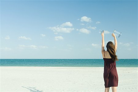 reaching sky - Woman standing on beach, holding up clear container, rear view Stock Photo - Premium Royalty-Free, Code: 632-01638580