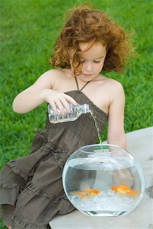 Redheaded little girl pouring bottled water into goldfish bowl Stock Photo - Premium Royalty-Free, Code: 632-01638594