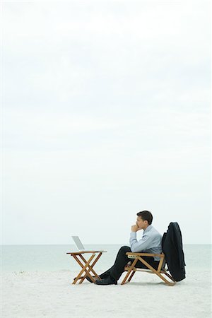 Businessman sitting in chair on beach, looking at laptop computer, side view Stock Photo - Premium Royalty-Free, Code: 632-01638676
