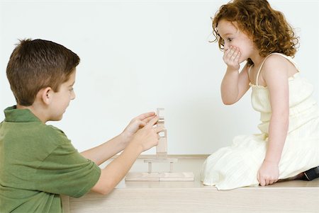 Boy stacking blocks while little sister watches, hand over mouth Stock Photo - Premium Royalty-Free, Code: 632-01785425