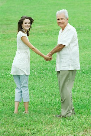 Grandfather and teenage granddaughter holding hands, both smiling over shoulders at camera Stock Photo - Premium Royalty-Free, Code: 632-01828388