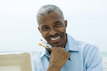 simsearch:696-03395223,k - Senior man holding paint brushes outdoors, smiling at camera, canvas in foreground Foto de stock - Sin royalties Premium, Código: 632-01828479