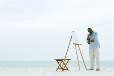 easel - Male painter standing in front of blank canvas at the beach, hand under chin, looking down Stock Photo - Premium Royalty-Free, Code: 632-01828490