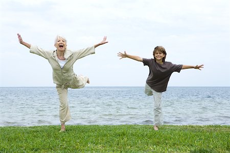 flying happy woman images - Grandmother and grandson standing on one leg, arms outstretched, both smiling at camera Stock Photo - Premium Royalty-Free, Code: 632-01828624