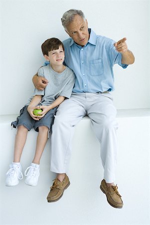 Man sitting with arm around grandson's shoulders, pointing, both looking away Stock Photo - Premium Royalty-Free, Code: 632-01828626