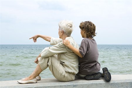 Grandmother and grandson sitting together by the sea, woman pointing, rear view Stock Photo - Premium Royalty-Free, Code: 632-01828652